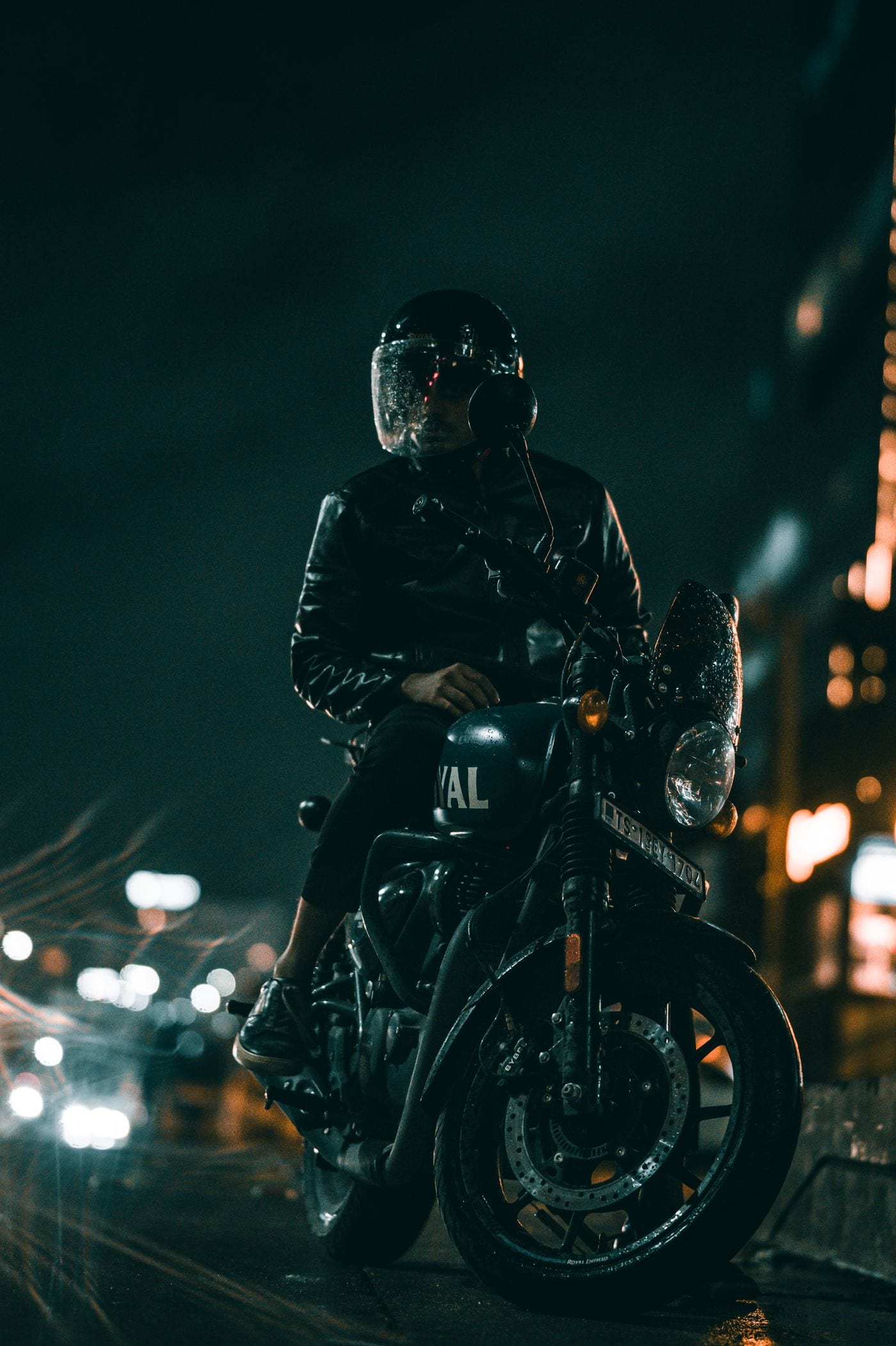 Motociclista parado em via urbana à noite, com luzes da cidade ao fundo