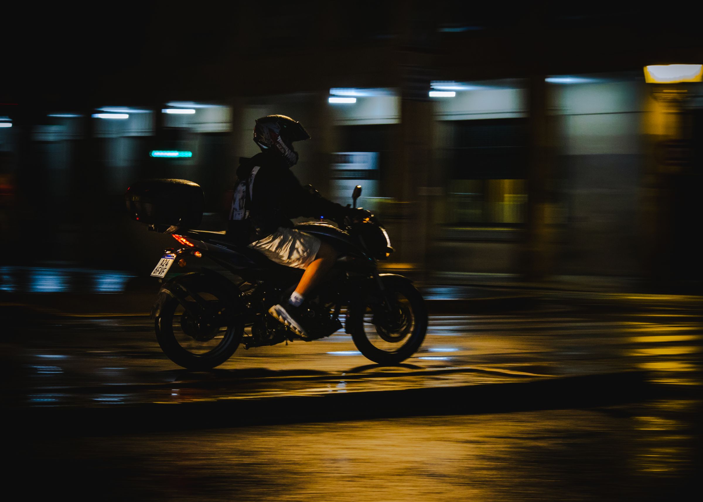 Motociclista em movimento em via urbana à noite, com rastros de luz ao fundo