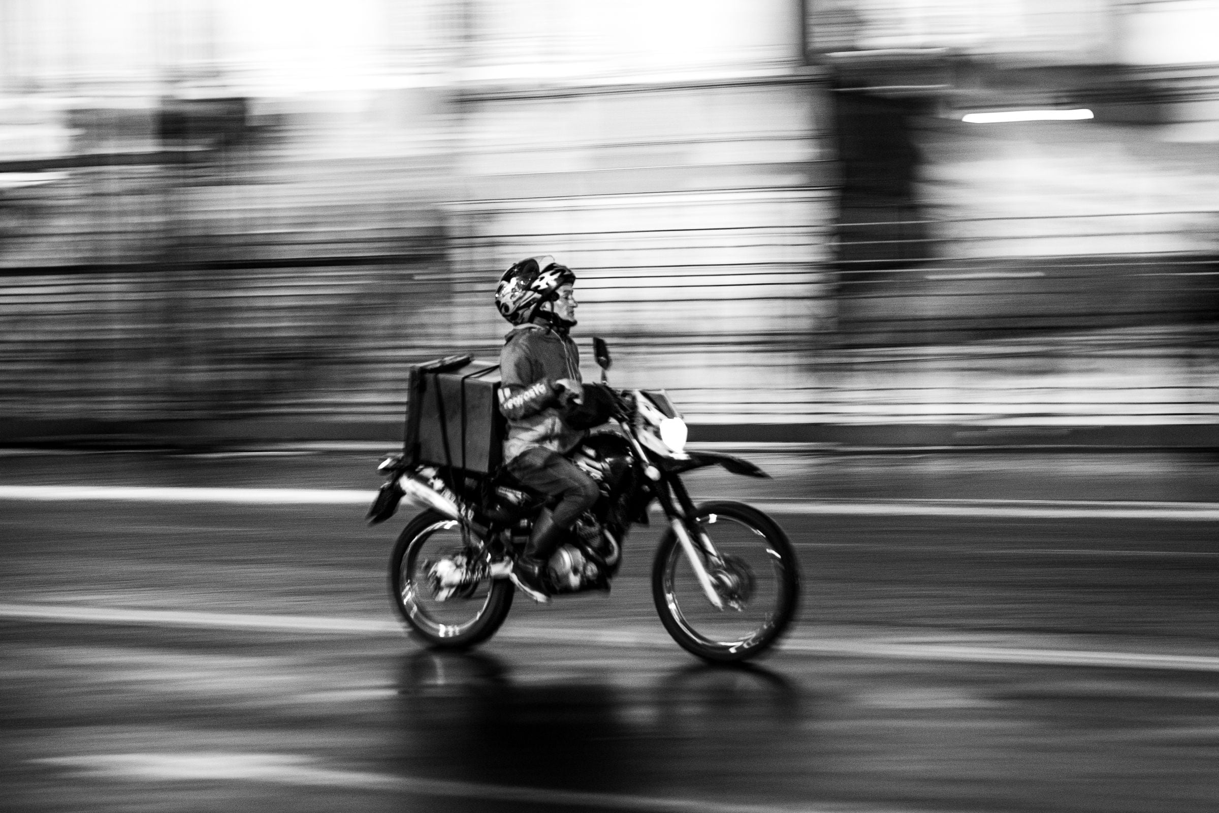 Entregador de moto em rua molhada, foto em preto e branco